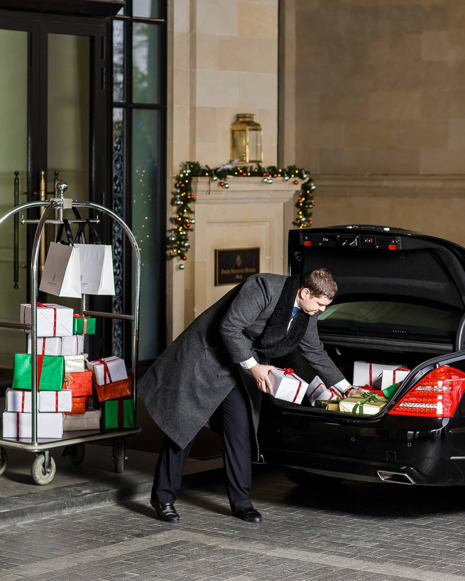 Suited man puts wrapped Christmas presents in luxury car trunk