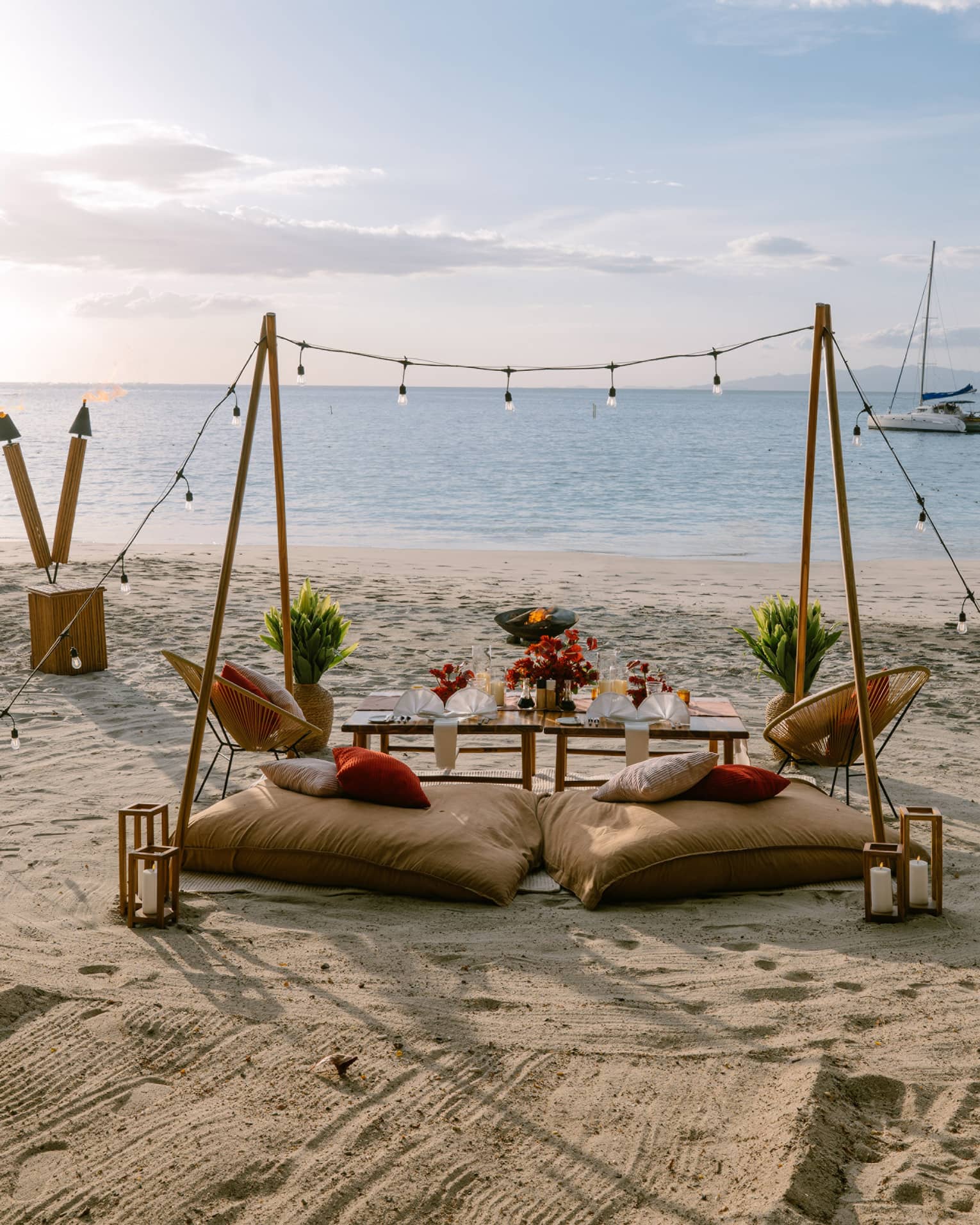 Private dining set up on a beach with two cusions, a table, string lights and rustic decorations