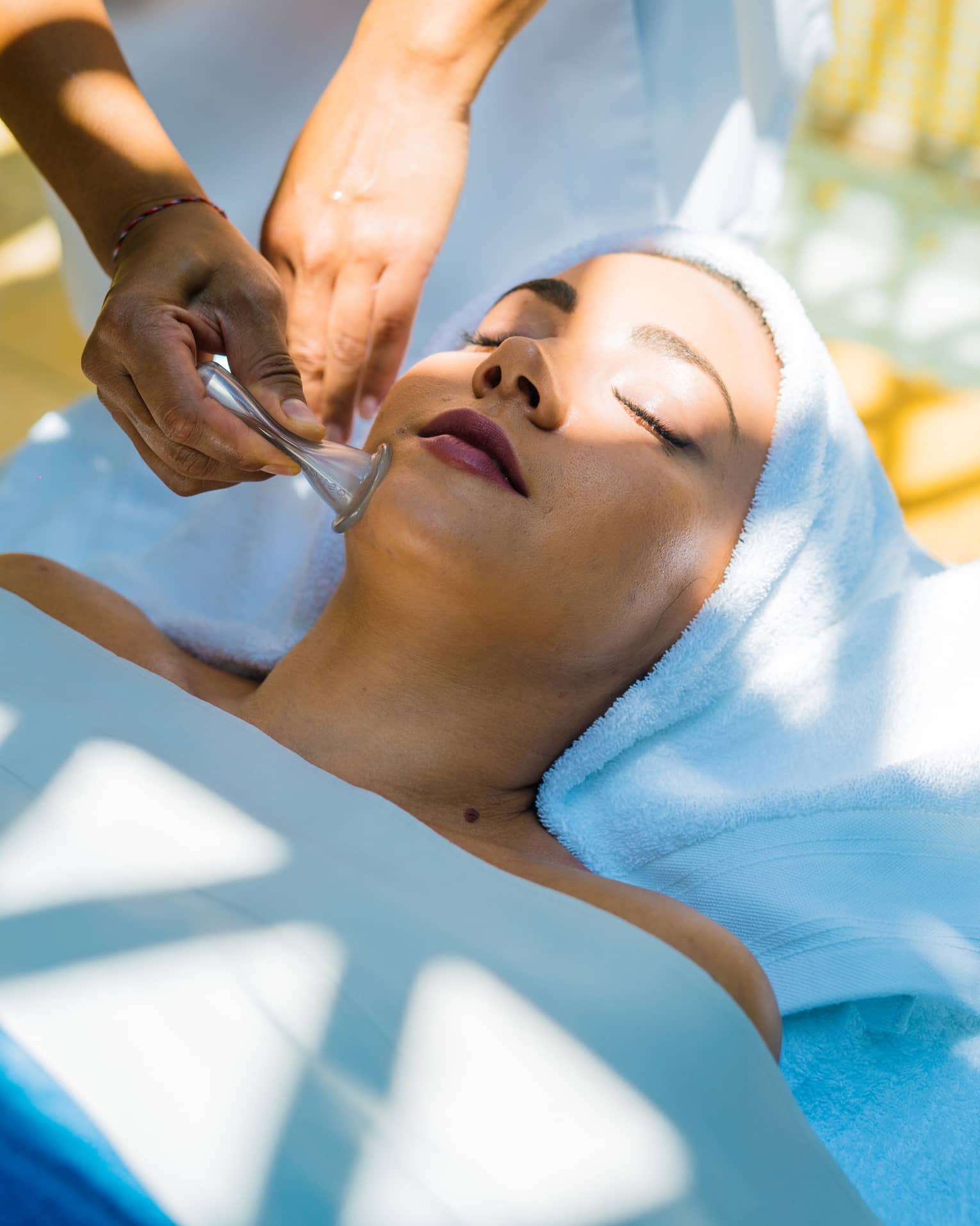A woman lays on a table as a masseuse uses a roller on her face.