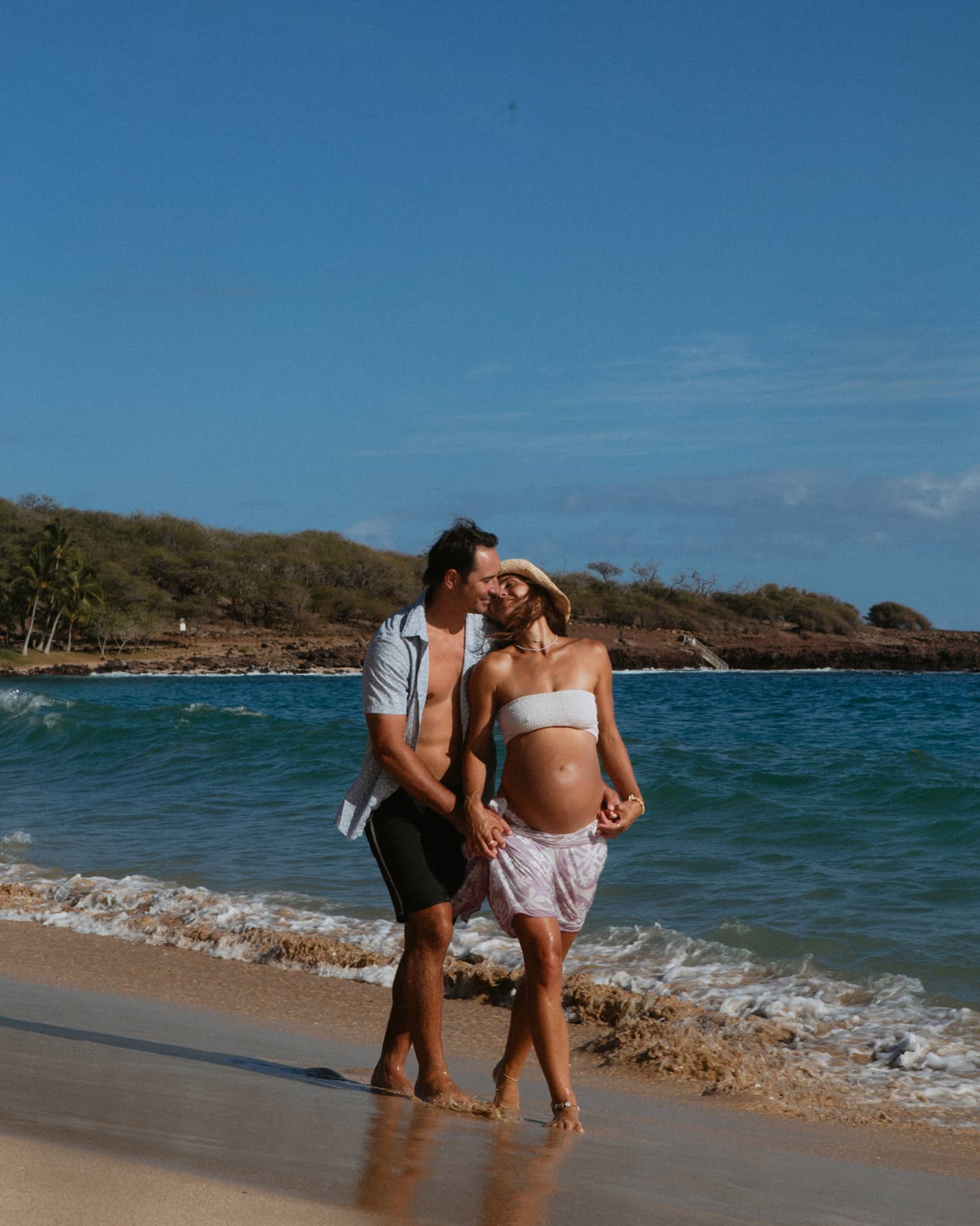 Man and pregnant woman walk together and embrace on the beach