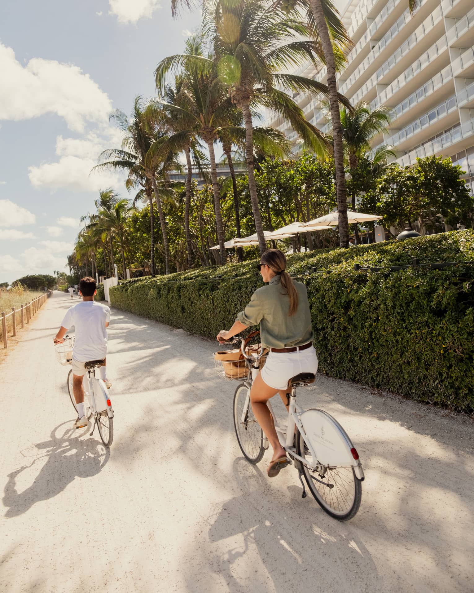 Two people ride bicycles on beach path