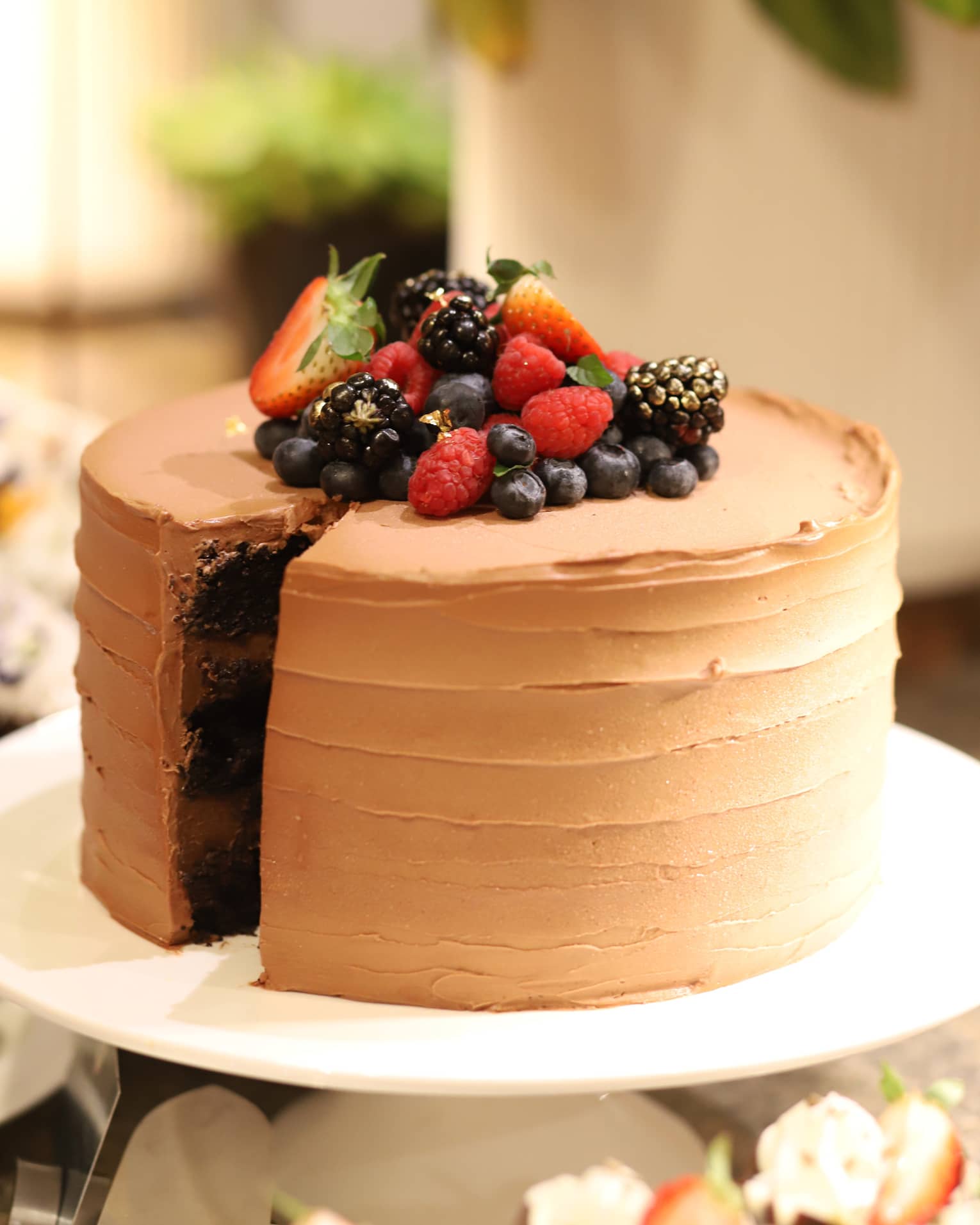 Round chocolate cake with chocolate frosting topped with fresh strawberries, blueberries, blackberries and raspberries