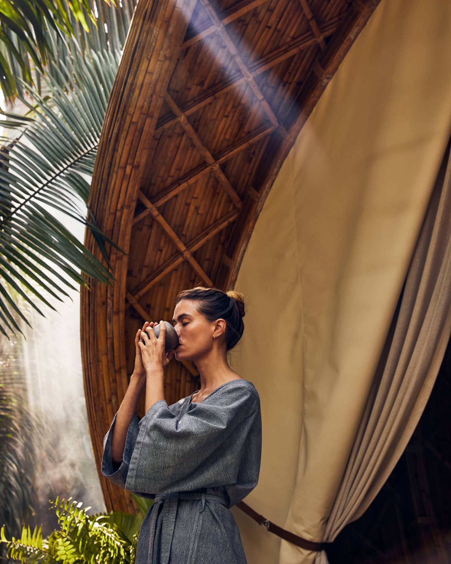 A woman drinking near palm trees and a large spa pod.