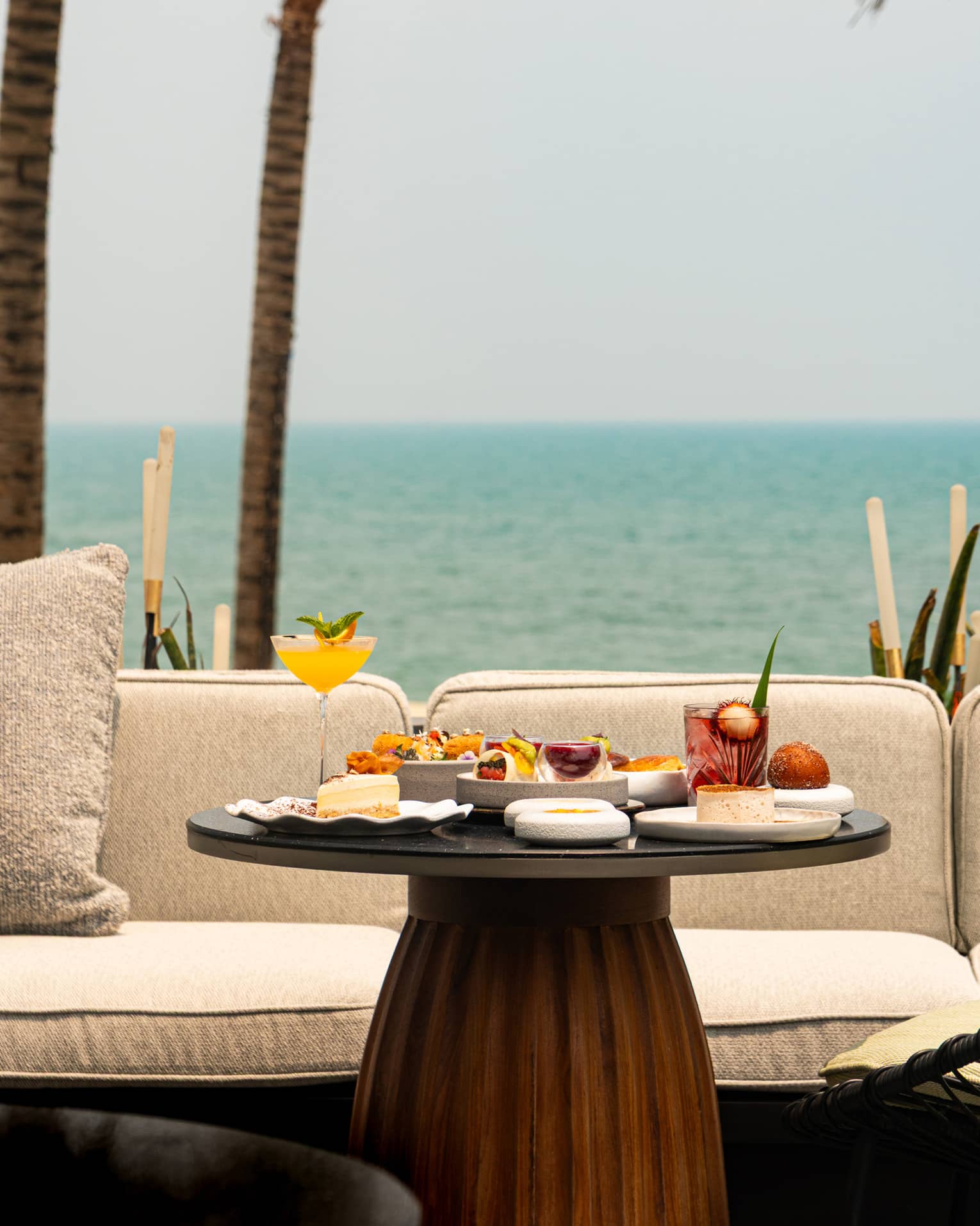 Round table set for afternoon tea in front of cream outdoor sofa, overlooking the sea