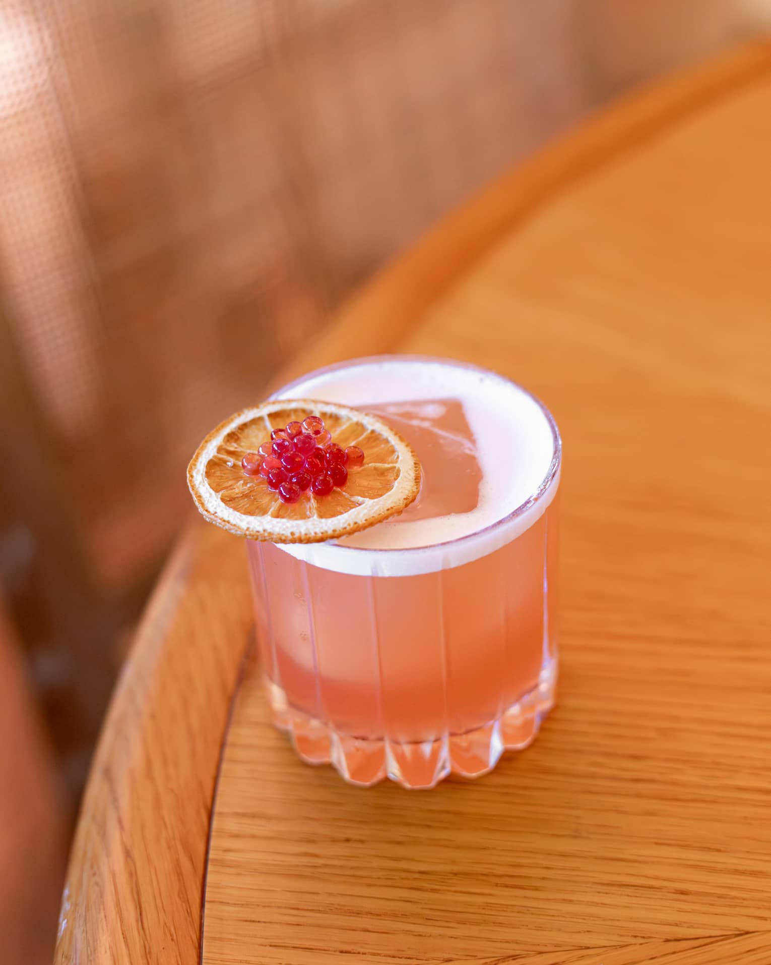 Coral-hued cocktail served in a rocks glass and garnished with an orange slice