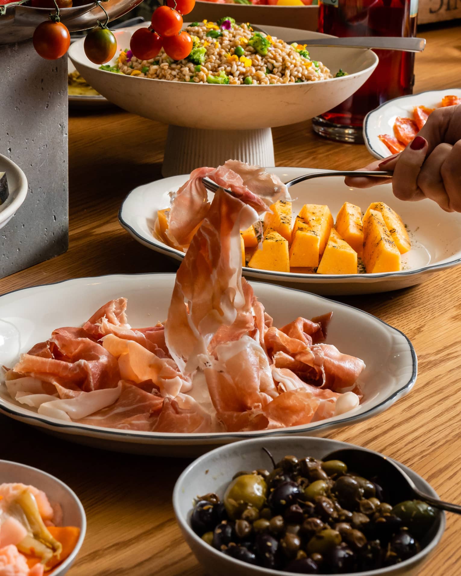 An aperitivo table laden with beautifully plated meats, olives and salads, a fork lifting a slice of prosciutto.