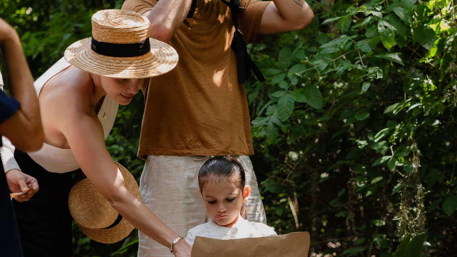A group of people on a jungle trail. Two are consulting a map, and one is looking through binoculars.