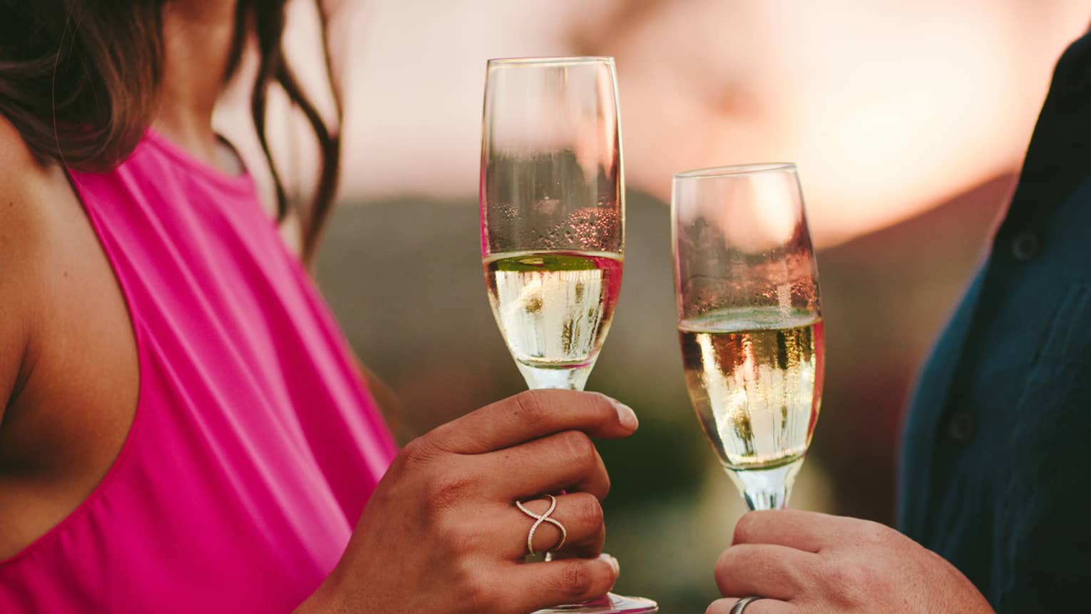 A woman in a fuscia pink dress hold a glass of champagne next to a man with a navy shirt holding his own glass 