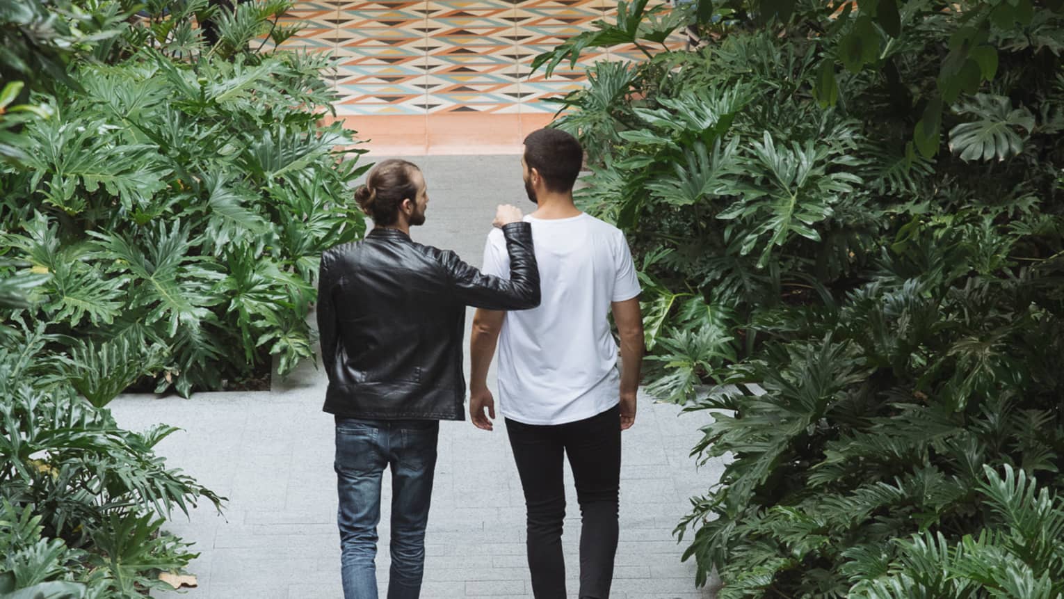 Two guests walking on an outdoor stone path leading to a dining room, surrounded by lush greenery