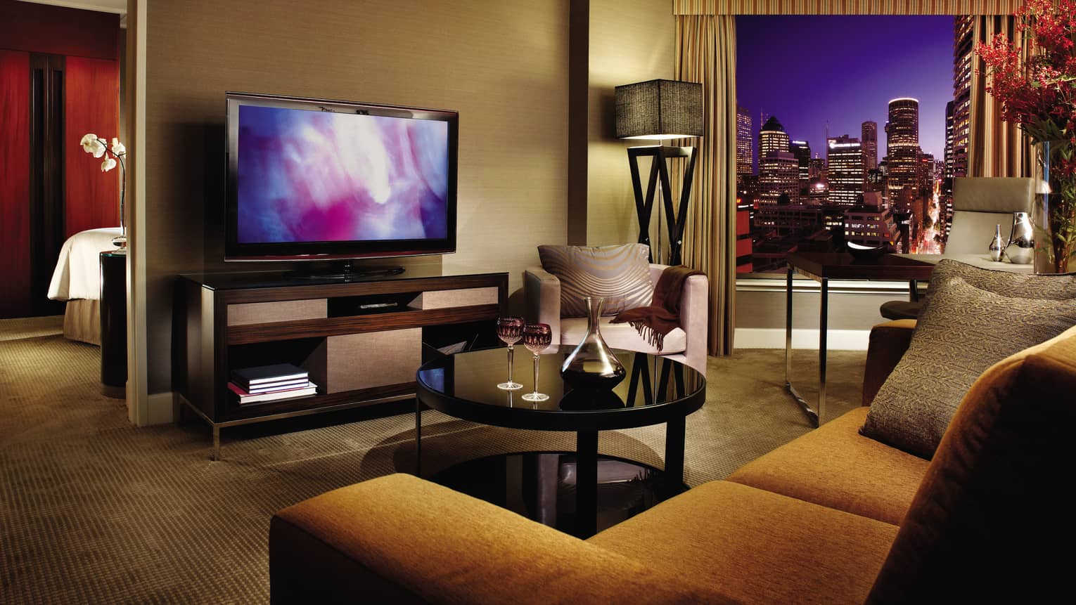 Club City Suite gold upholstered sofa, table with wine glasses, TV, bedroom door at night