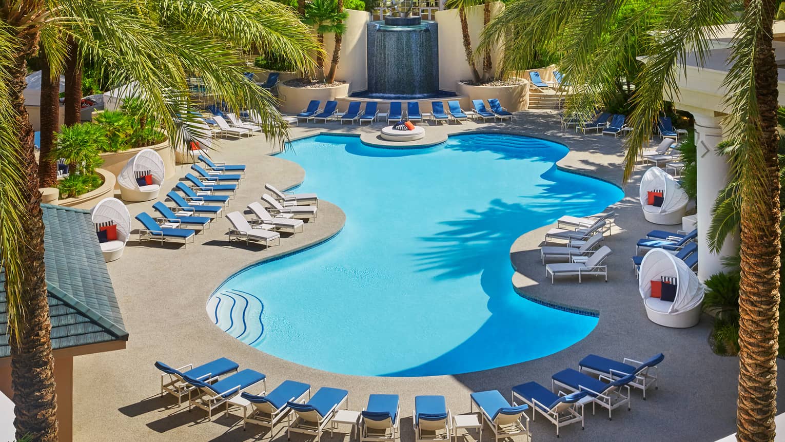 Waterfall in front of blue lounge chairs, curved outdoor swimming pool