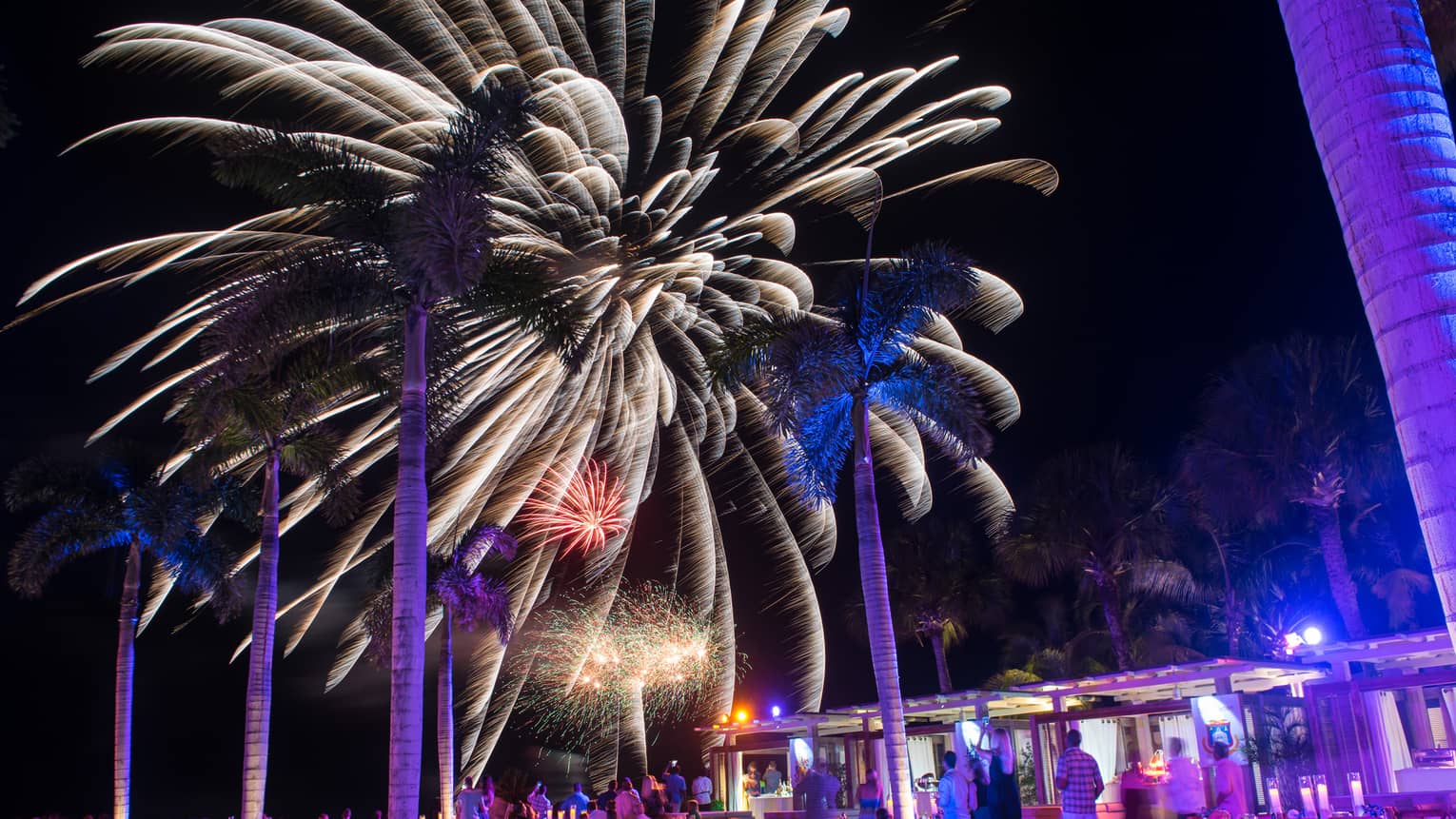 People around resort outdoor pool/bar watching fireworks in the night sky