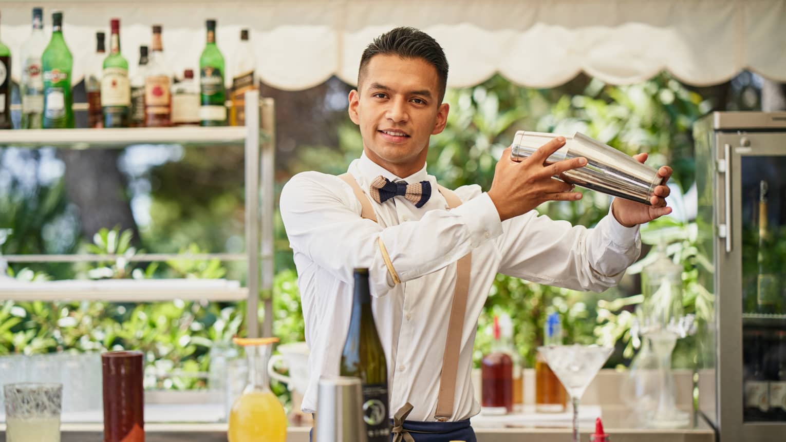 Barman Frank Carcamo standing behind outdoor bar, shaking a cocktail