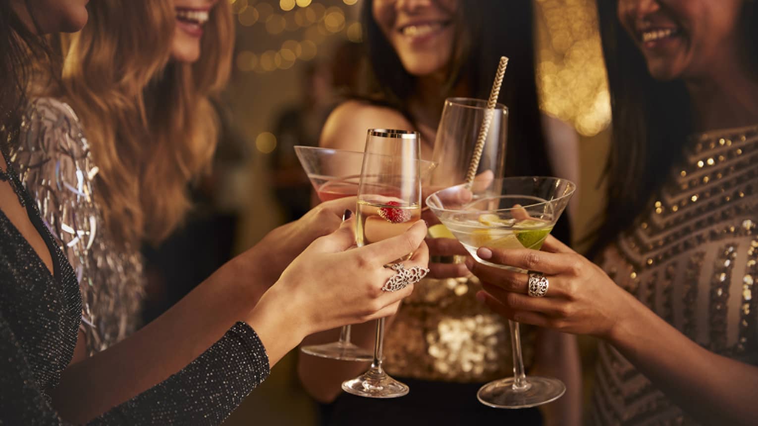 Four women in evening wear clink their cocktail glasses