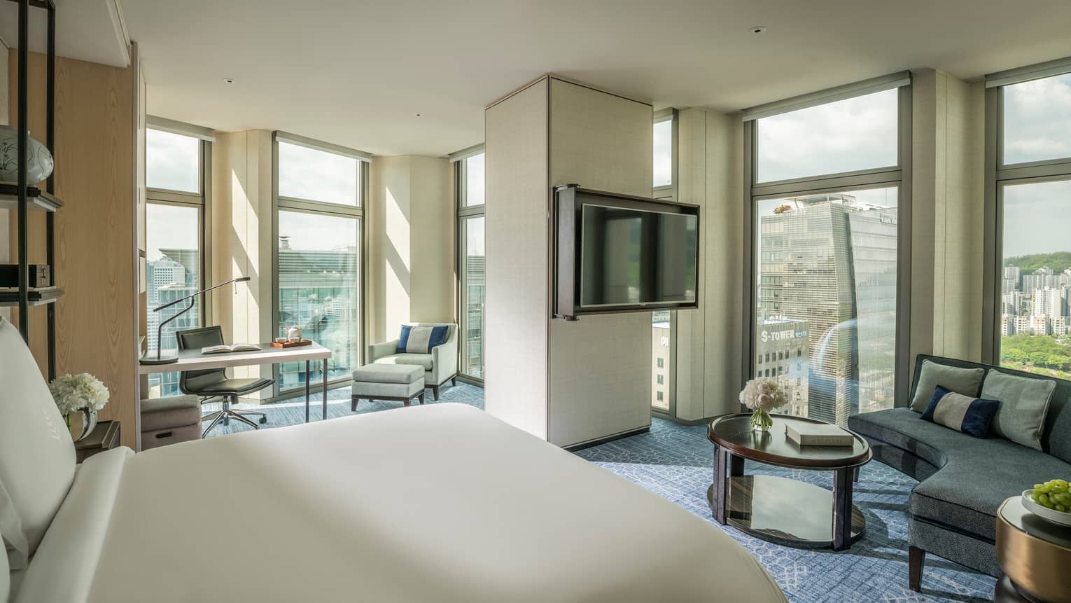 Corner Premier Room across from curved sofa by windows, TV on pillar separating work desk, armchair