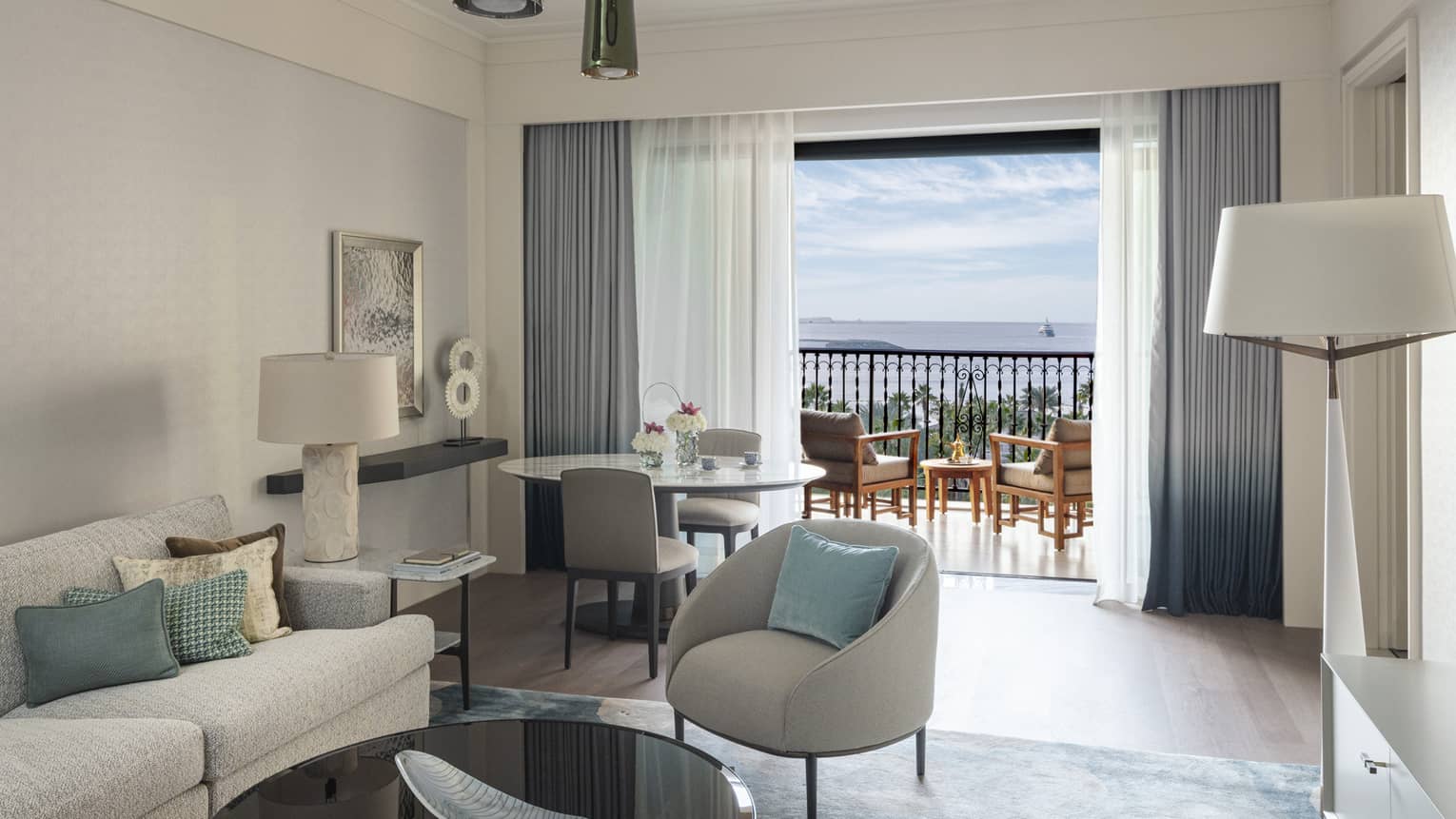 Living room of a hotel suite, with a sofa, arm chair, round table and two chairs, and a walk-out balcony
