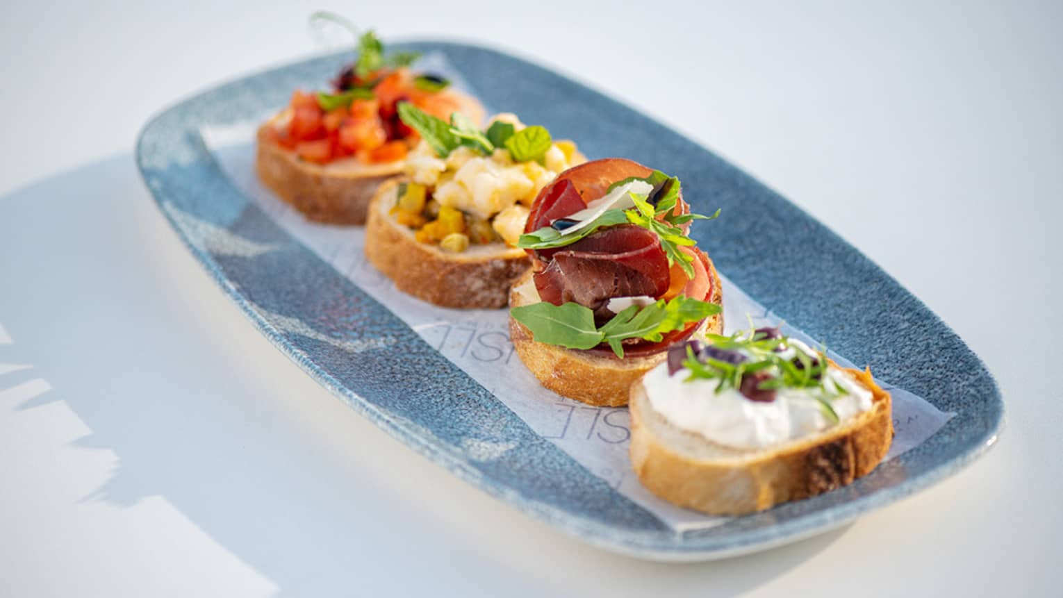 Four slices of Bruschetta with olives and tomatoes on top, all served on a grey platter.