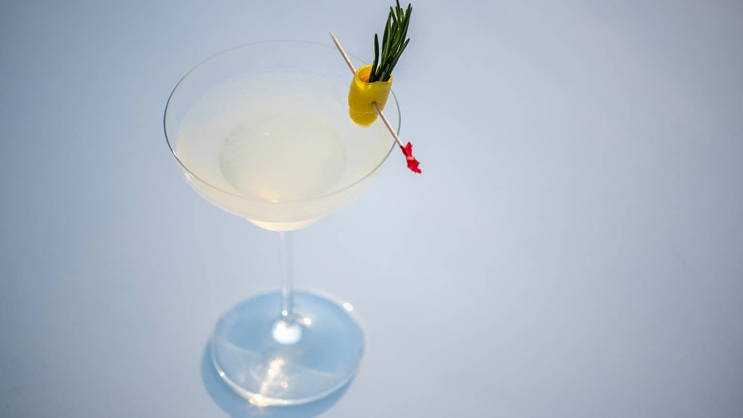 A yellow cocktail in a martini glass with an olive topping the glass.