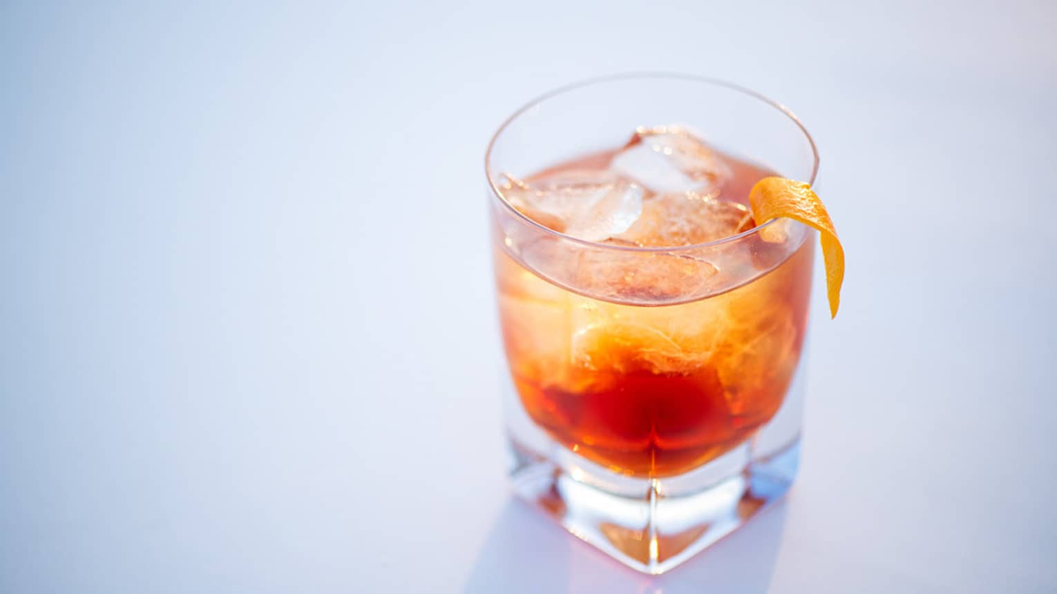 A blood orange cocktail in a whiskey glass and topped with an orange slice.