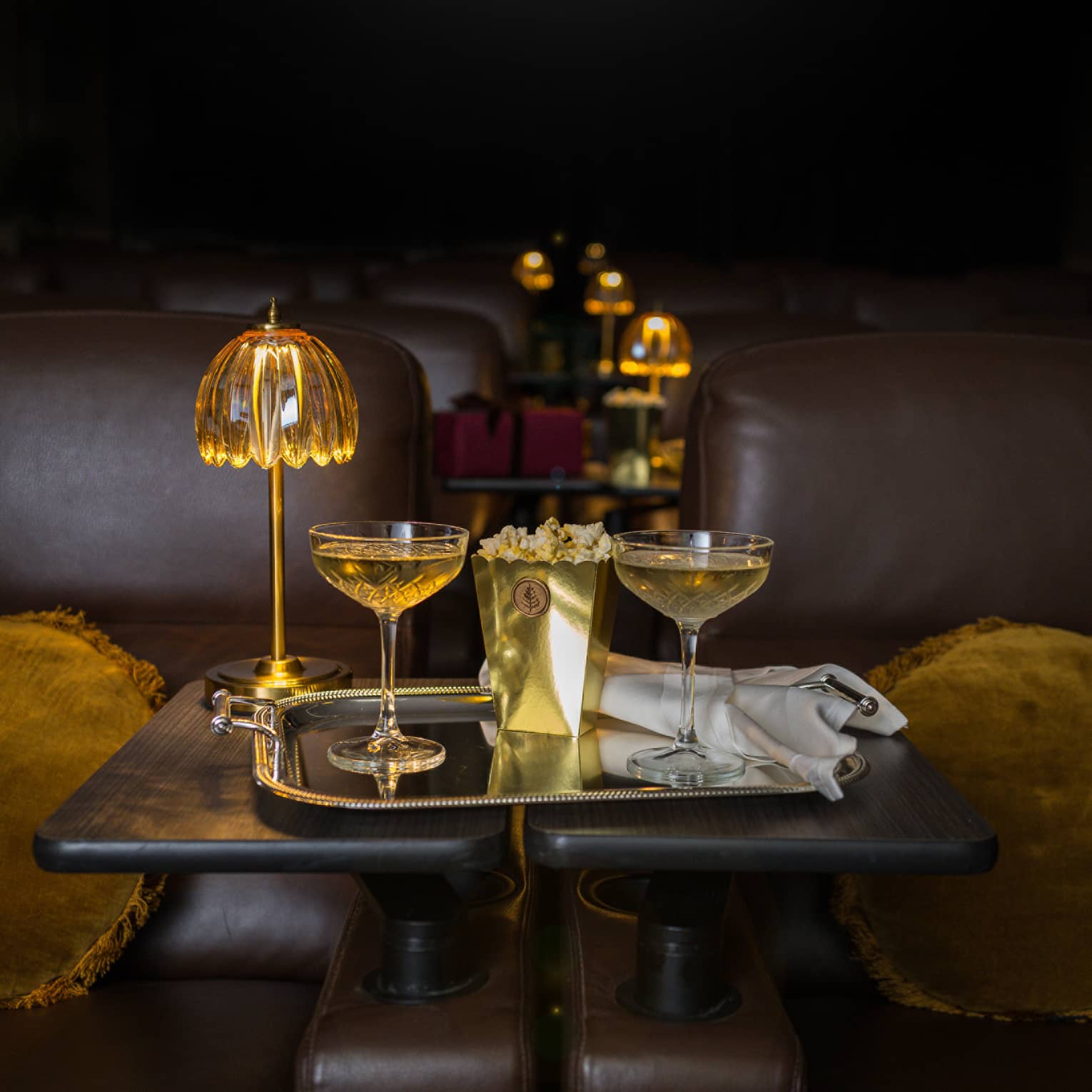 Two filled coupe glasses on a silver serving tray with popcorn in front of a golden dome light.