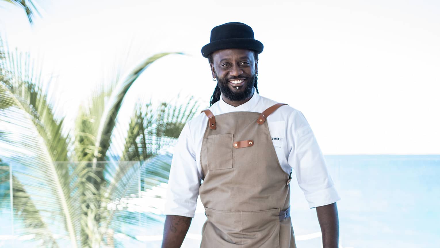 A chef in a brown apron standing near a beach outside.