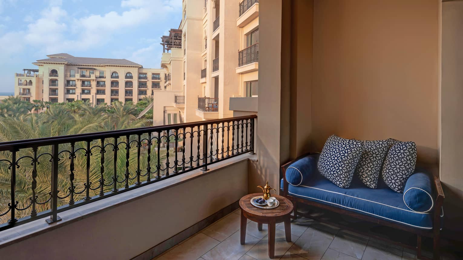 Private terrace with small blue sofa, small wooden table, overlooking palm trees