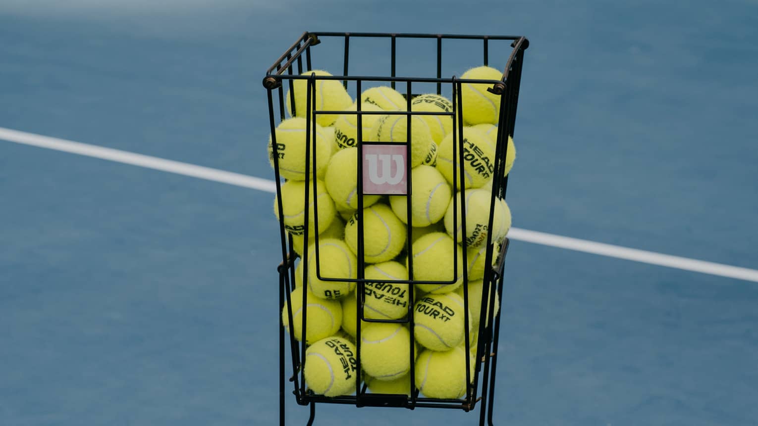 A basket of tennis balls on a blue tennis court