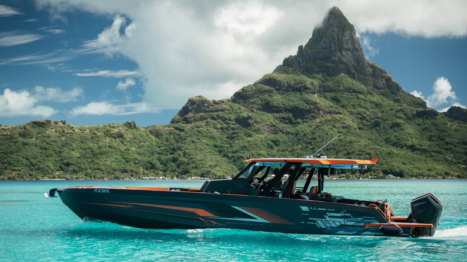 An orange and black yacht charter boar sails in front of a mountain landscape