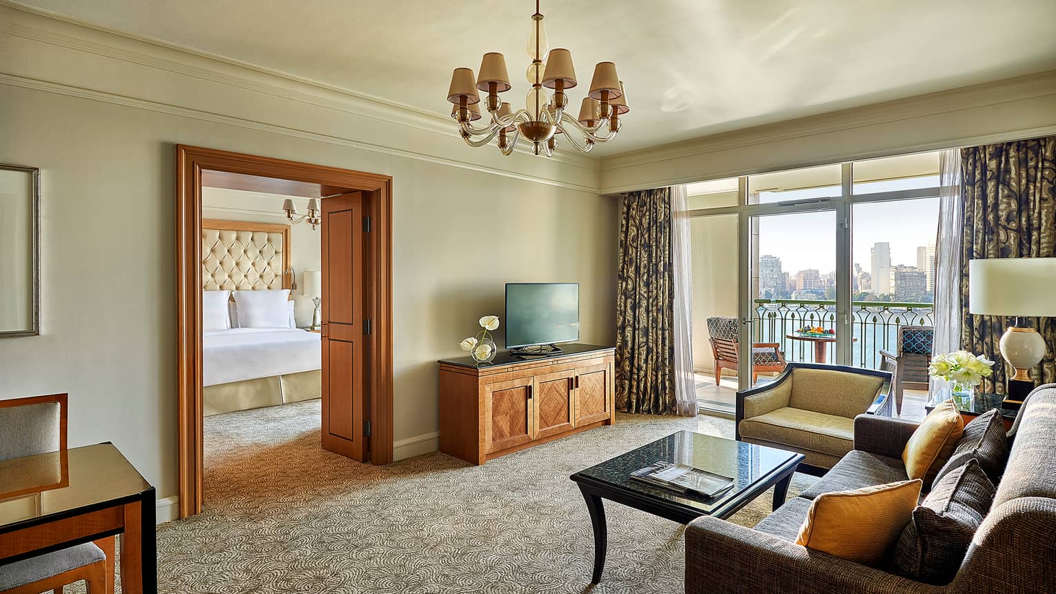 Suite living area with sofa, TV and coffee table, looking into adjoining bedroom at bed