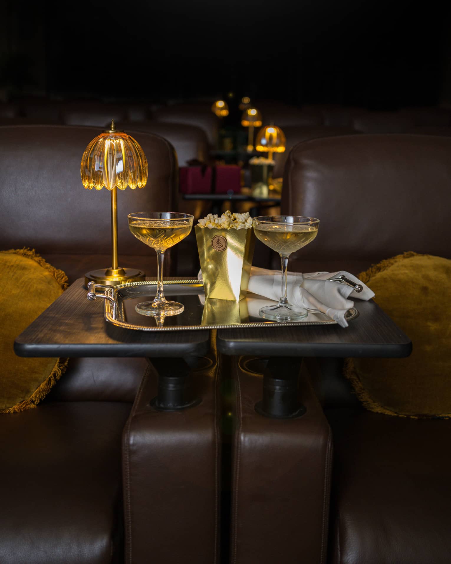 Two filled coupe glasses on a silver serving tray with popcorn in front of a golden dome light.