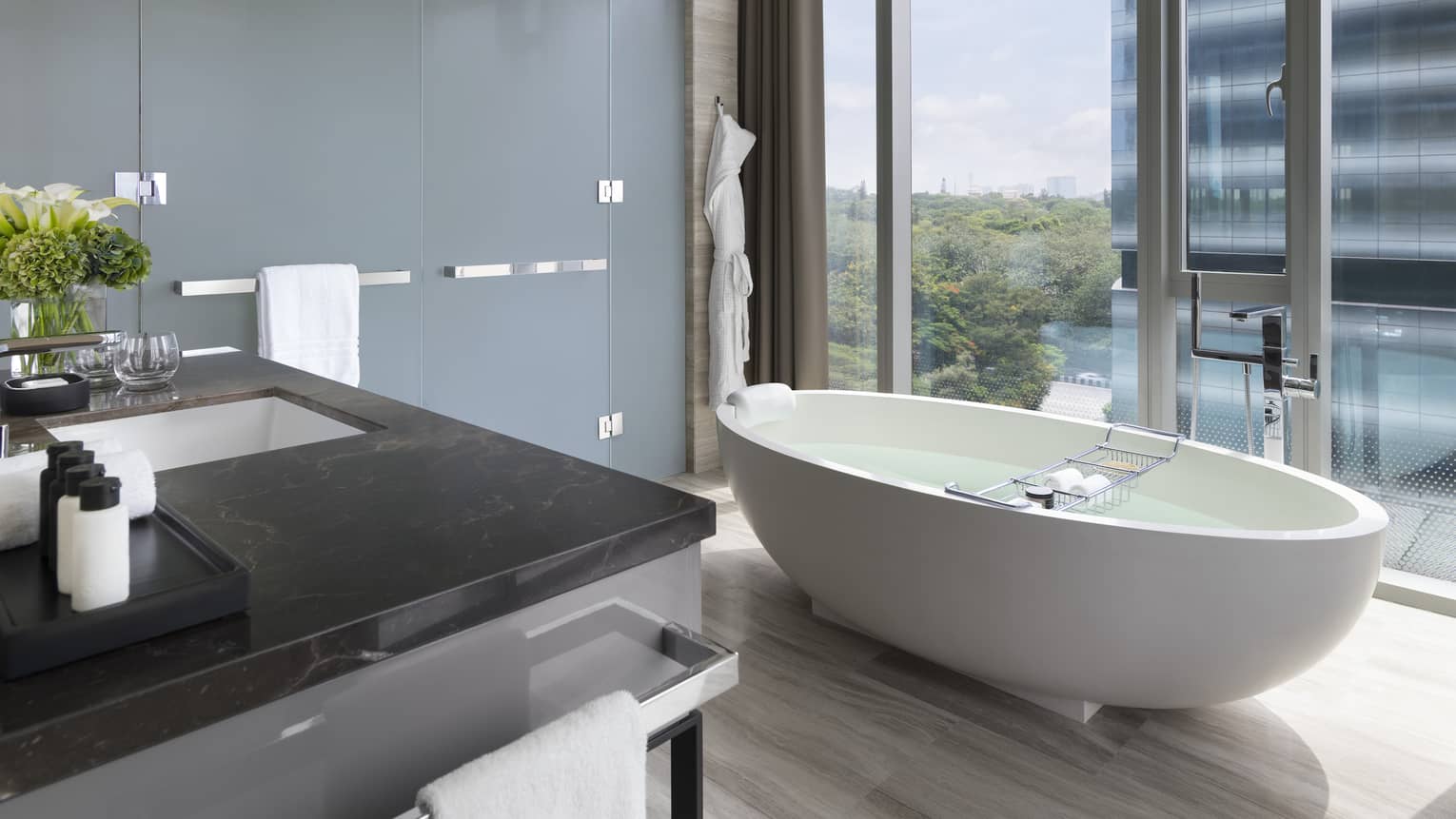 Bathroom with white free-standing tub set next to a floor-to-ceiling window