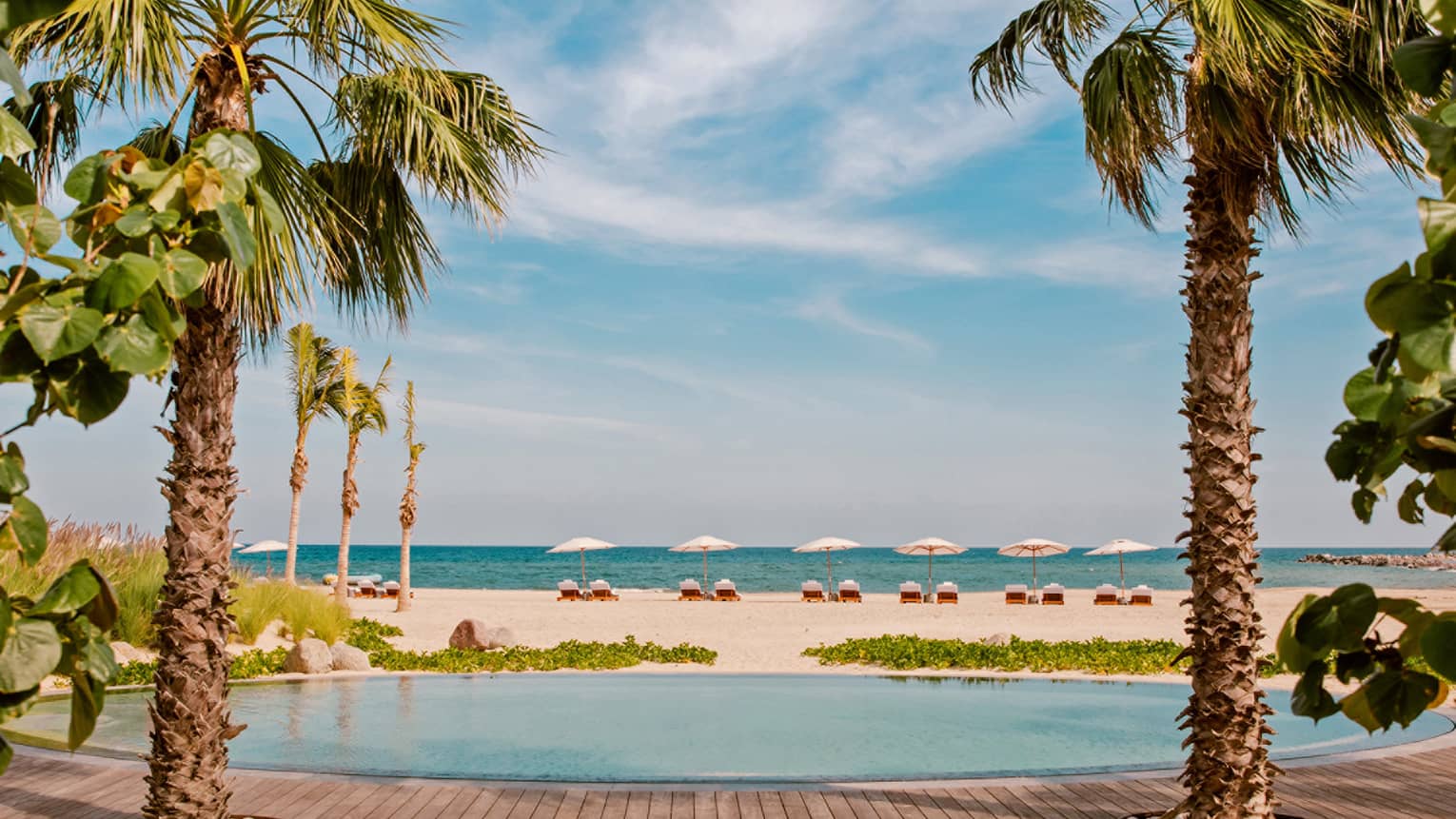 A round pool next to a white sand beach and palm trees.