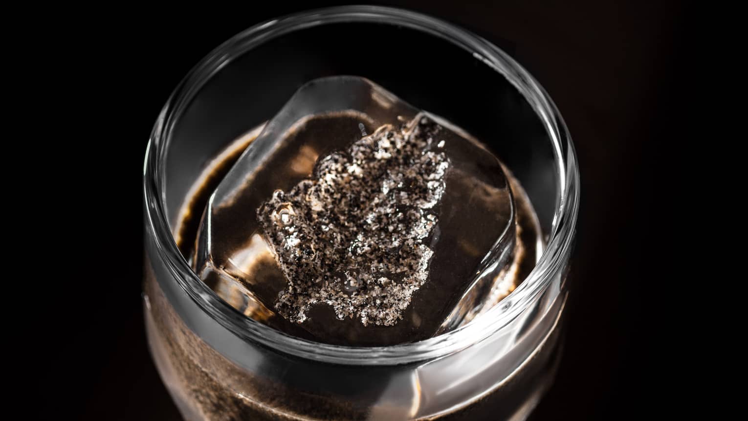Cocktail in clear glass on dark tabletop with Four Seasons leaf?shaped ice cube