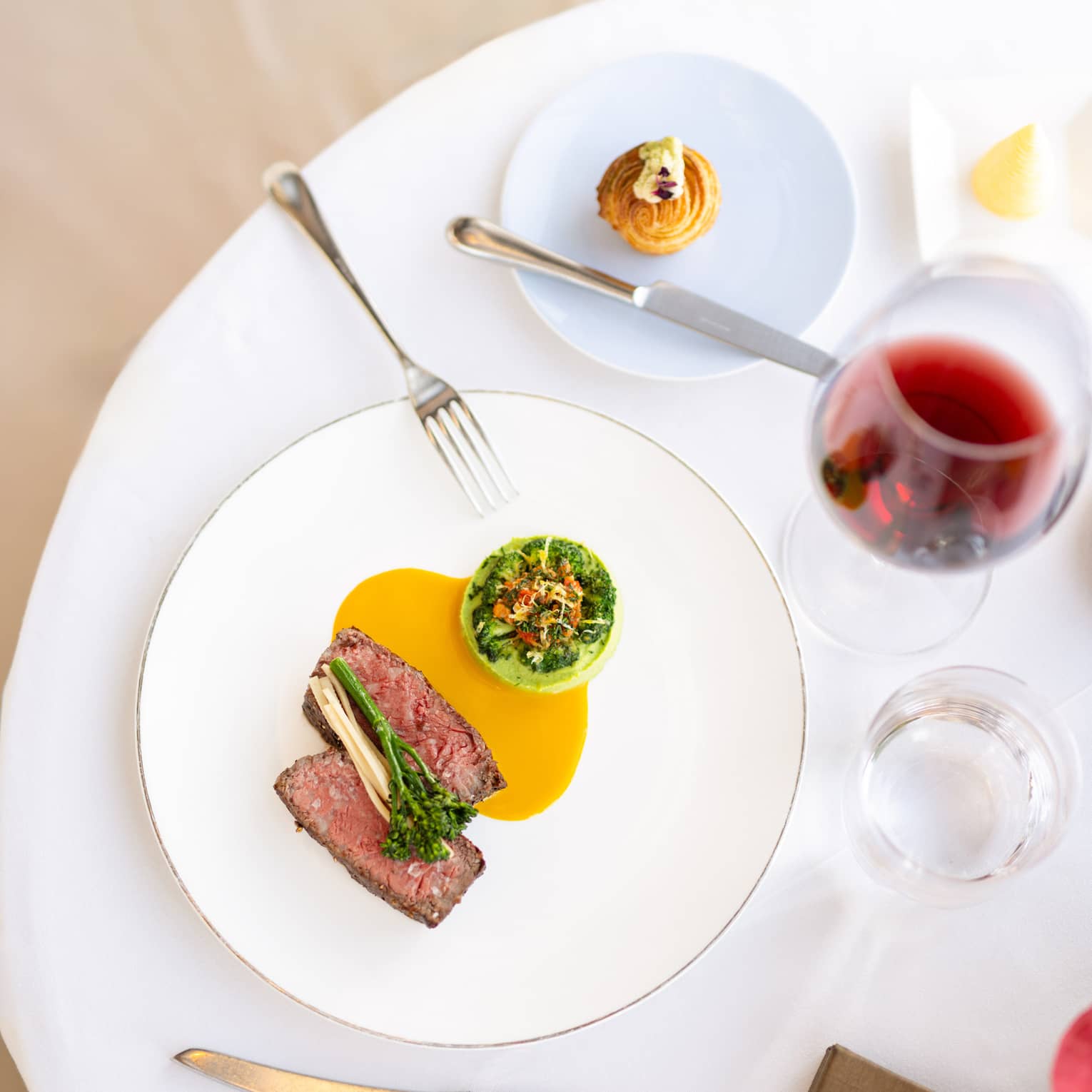 Sliced filet of steak served on a white plate with an orange-coloured sauce and a green vegetable side dish