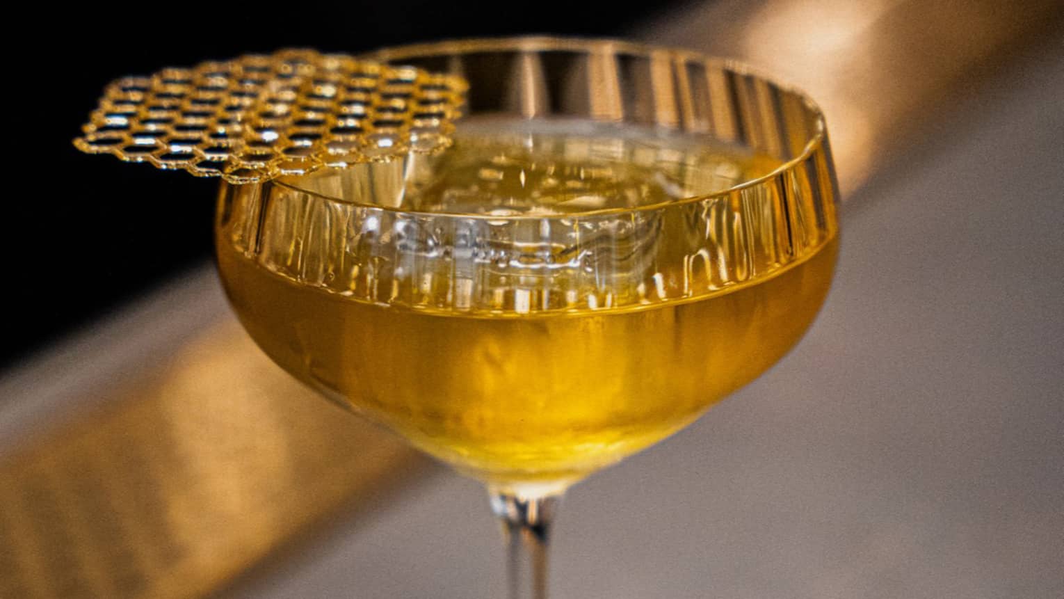 A cocktail with a golden color in a clear stemmed glass