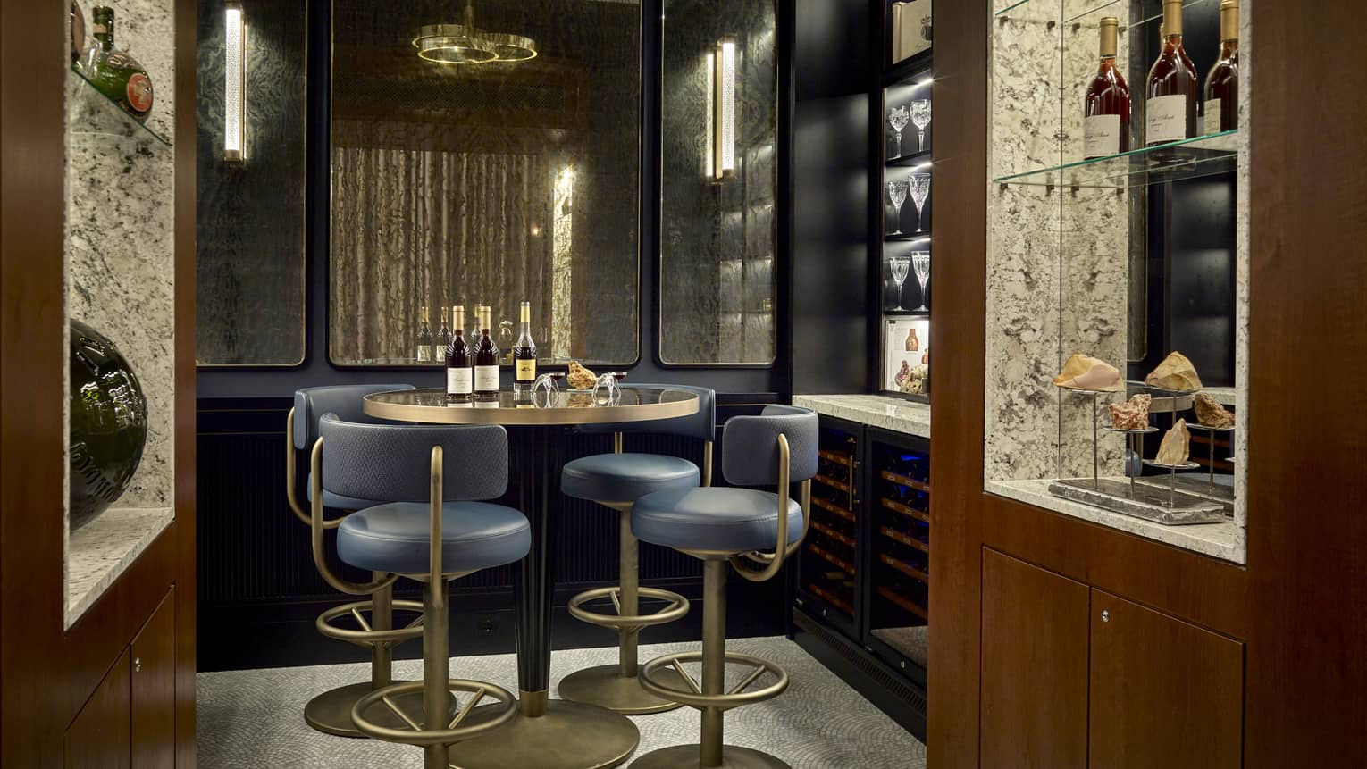 Dark private lounge area with navy and gold barstools at round high-top gold table, wine bottles