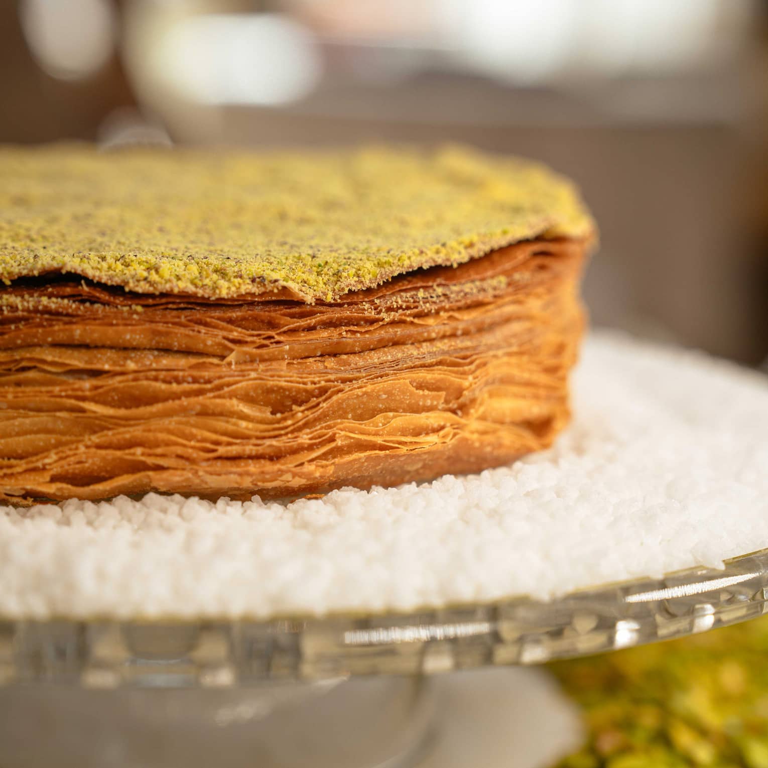 Close up of multi-layered pastry cake surrounded by white powdered sugar on a glass cakestand