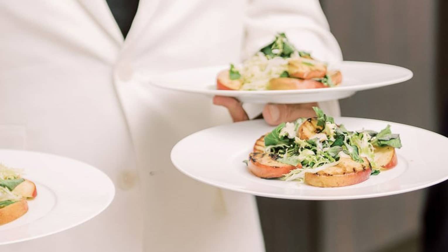 A waiter holding three plates of salad.