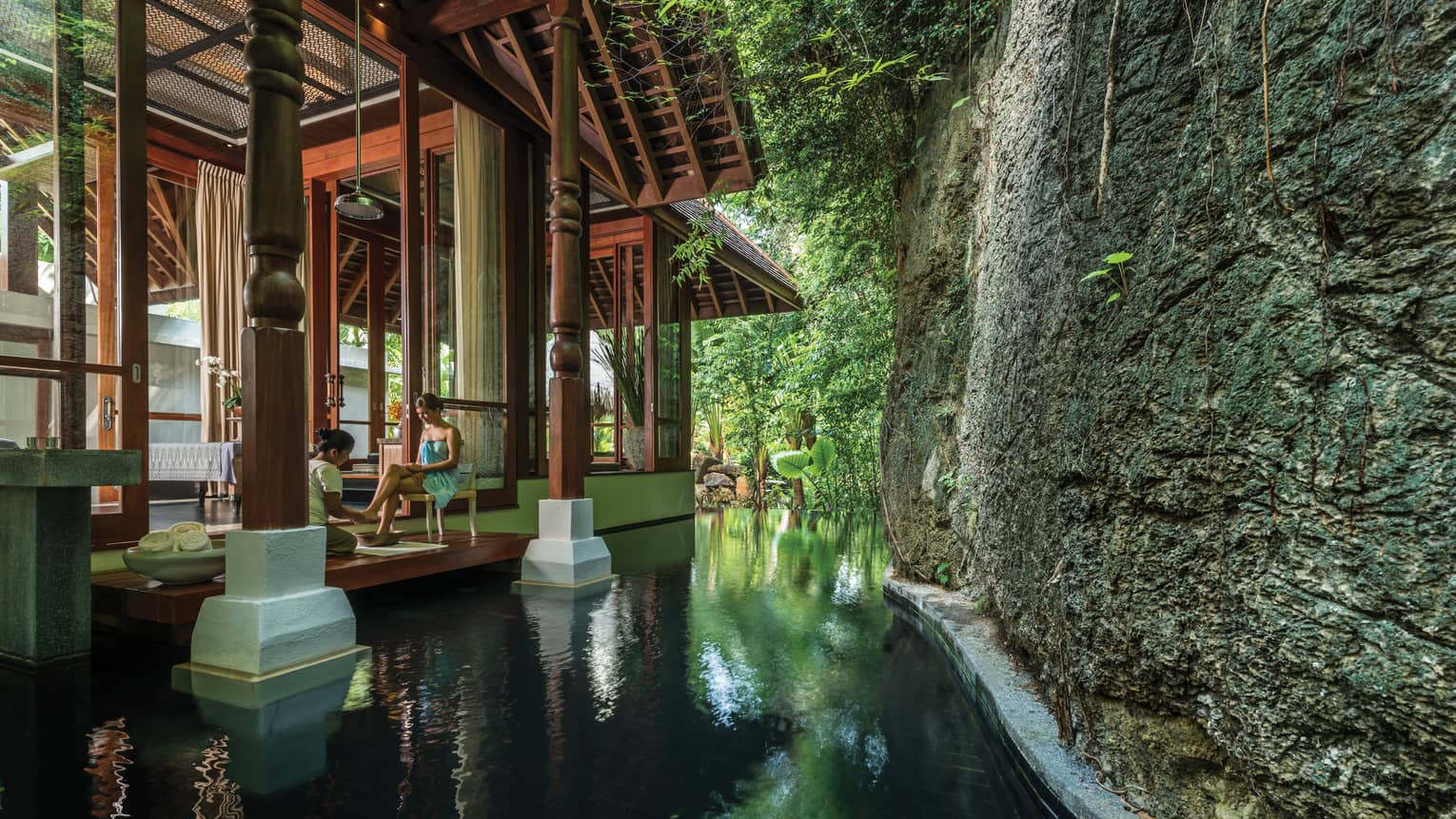 Woman gets foot massage on deck of Geospa by pool, large rock wall