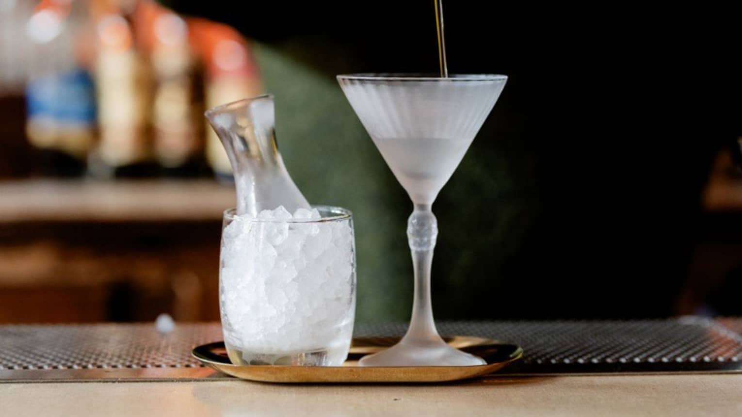 A bartender pours a clear cocktail from a shaker into a stemmed martini-style glass.