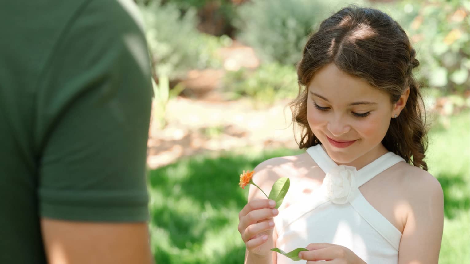 Child holding an orange flower while standing on lawn with nature guide wearing a green shirt