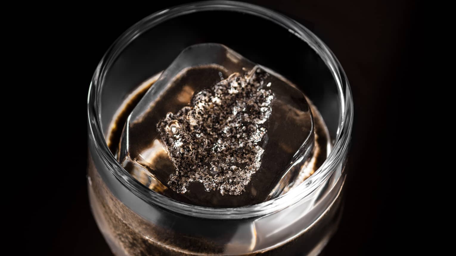 Cocktail in clear glass on dark tabletop with Four Seasons leaf?shaped ice cube