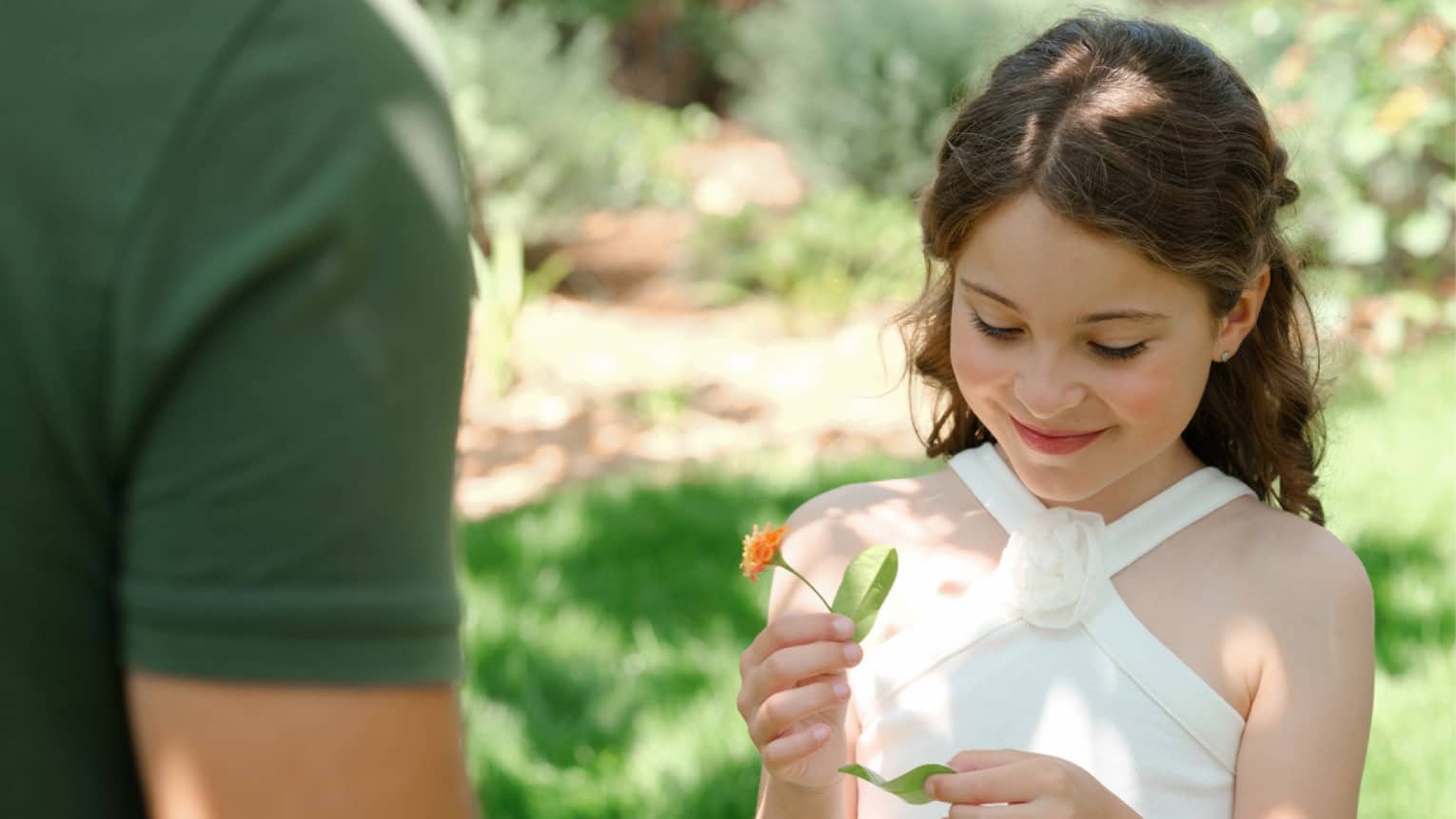 Child holding an orange flower while standing on lawn with nature guide wearing a green shirt