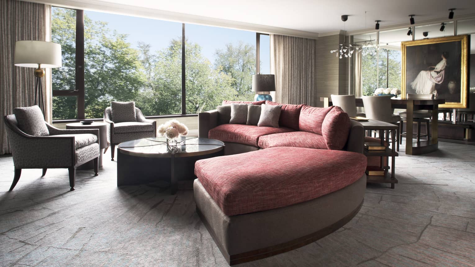 A large circular couch sits at the center of a well lit room, an intricate painting hangs in the background 