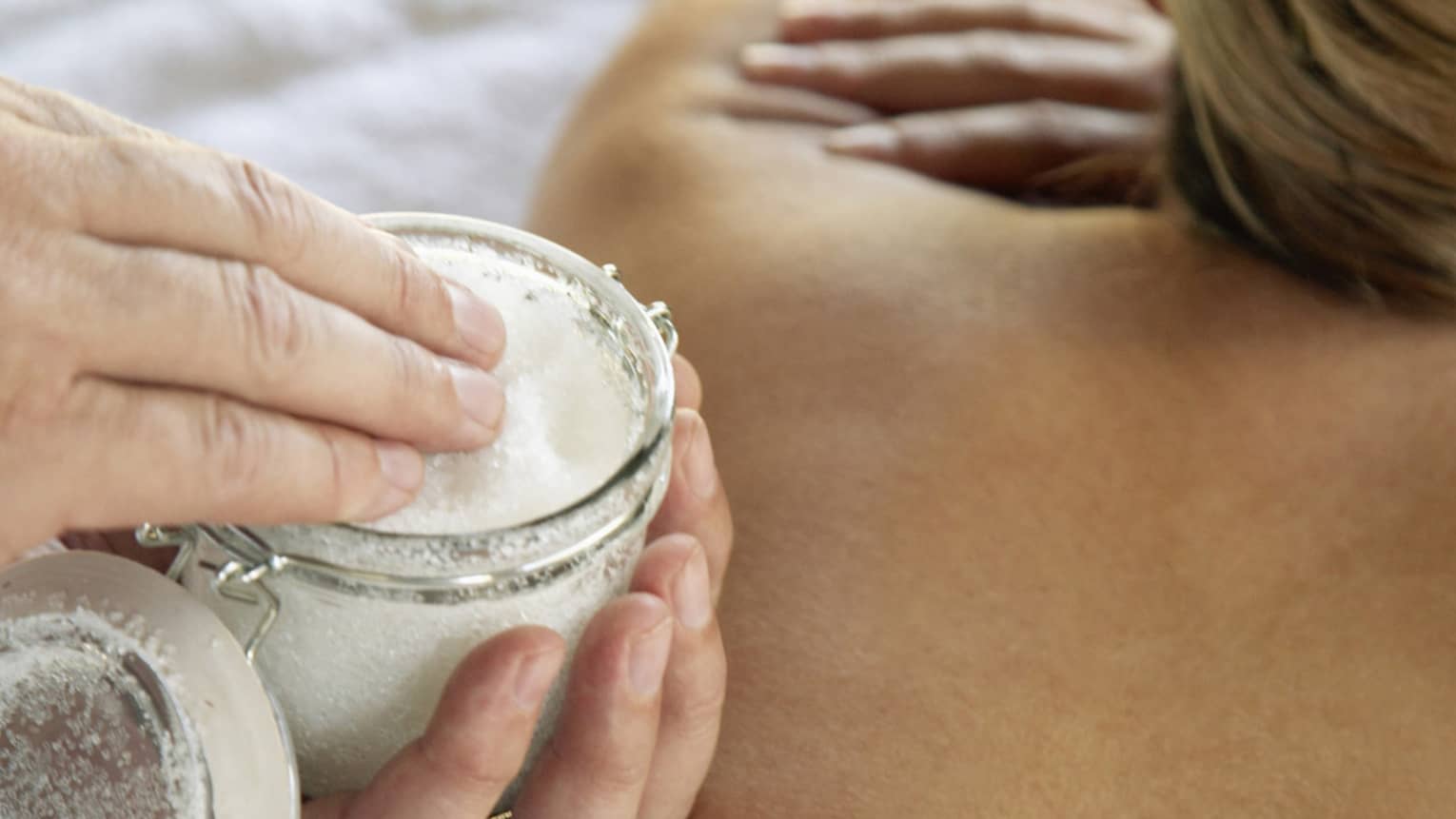 Jar of sea salt scrub above woman's bare back in spa