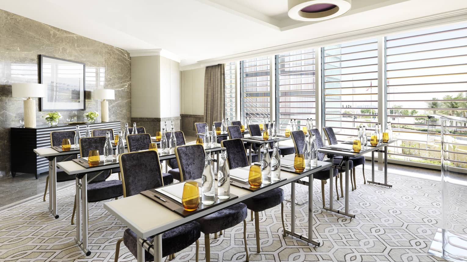 Three rows of modern tables with amber glasses, velvet chairs in the Al Maqtaa Meeting Room