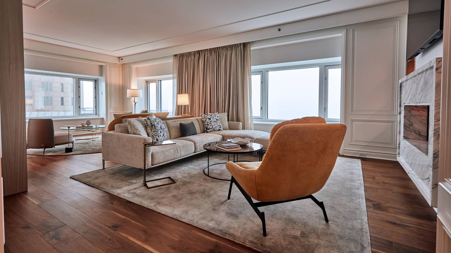 Living room with orange suede accent chair, beige sofa, round coffee table, windows and hardwood floors