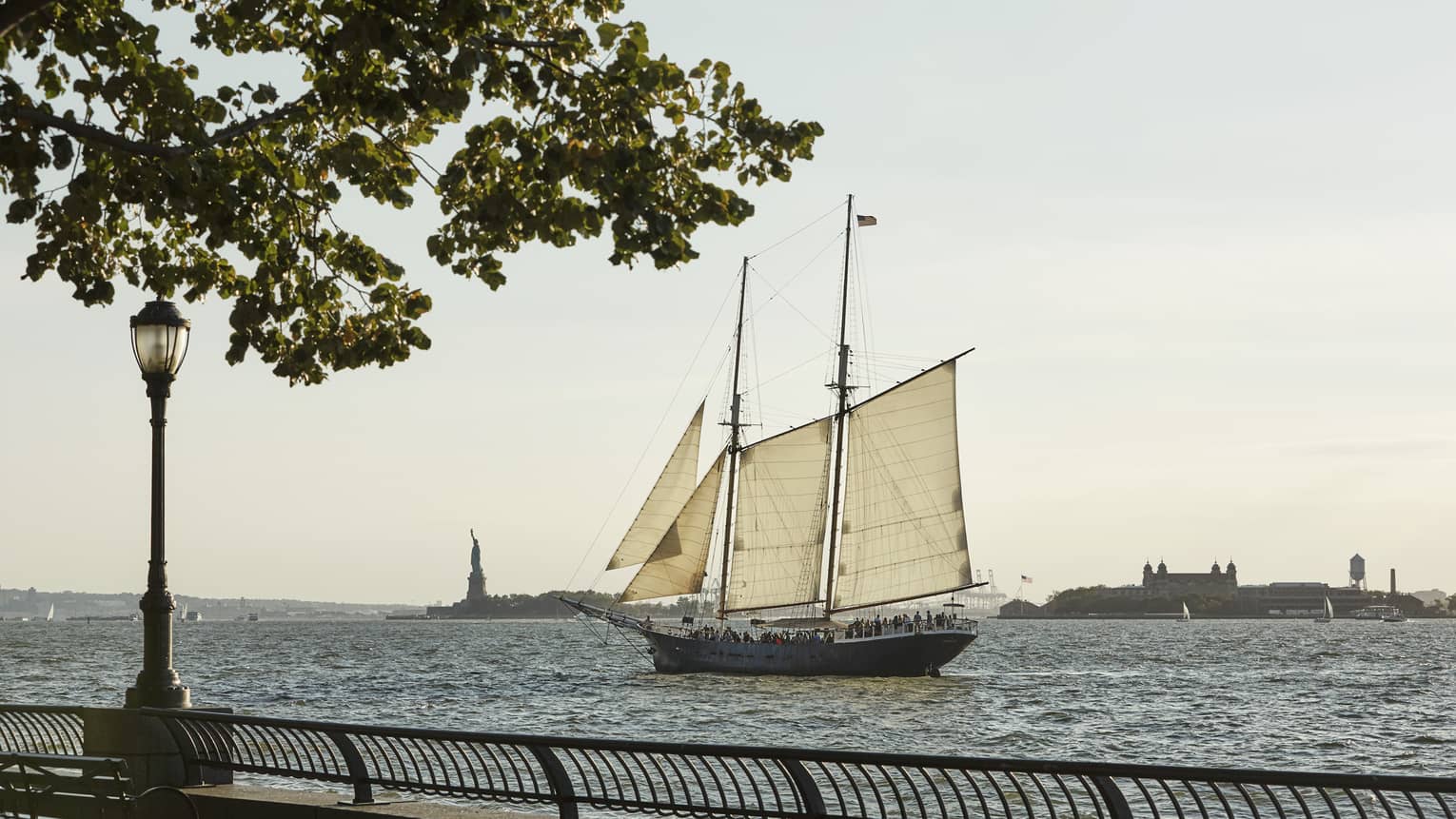 View from boardwalk as sailboat glides past Statue of Liberty in river 