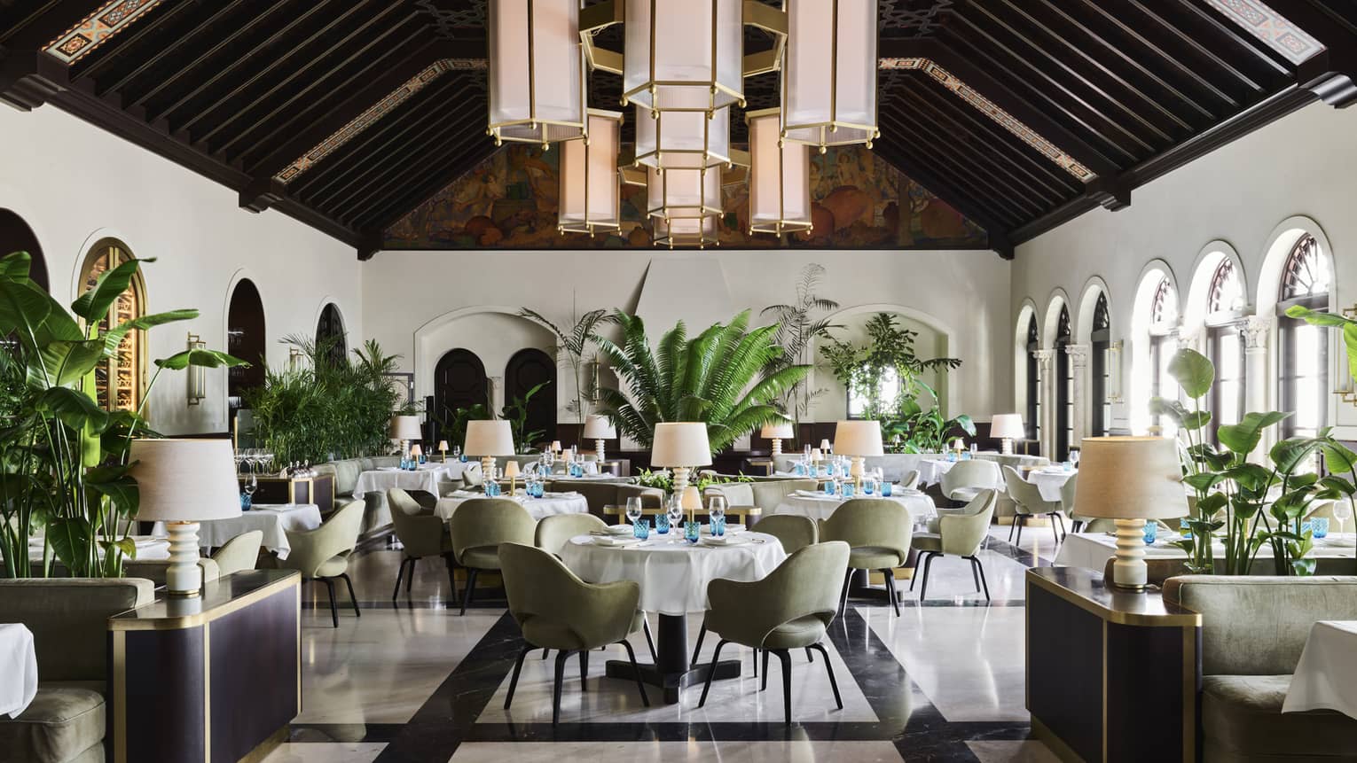 Light-filled restaurant with white walls, windows, dark wooden beams on pitched ceiling, hanging lantern-style lights