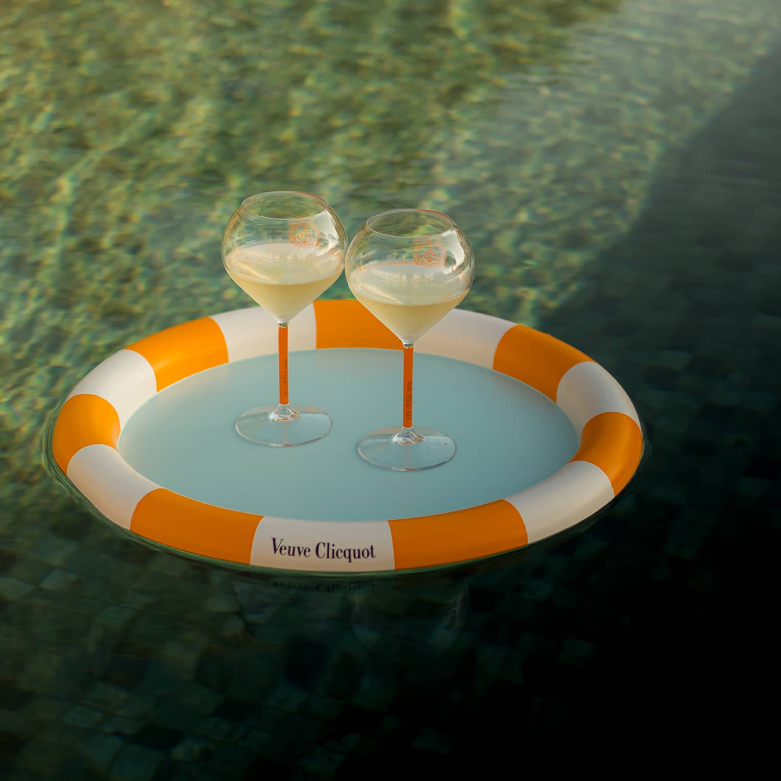 Two glasses of Veuve Clicquot served on a branded orange-and-white tray floating on the water